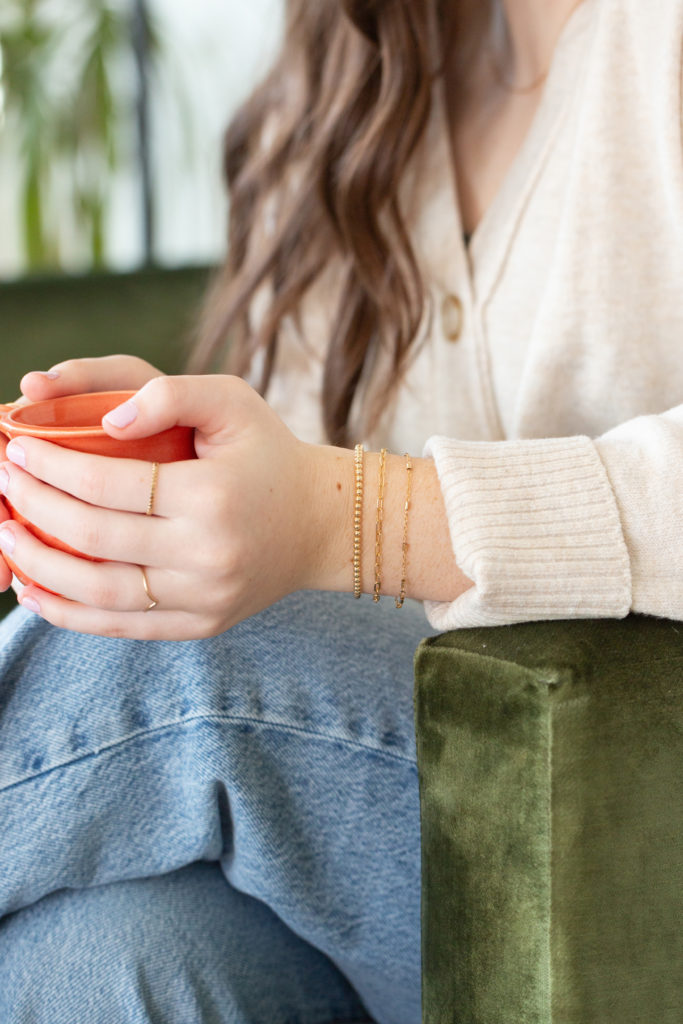 teen holds coffee cup while displaying permanent jewelry in Alma, Michigan
